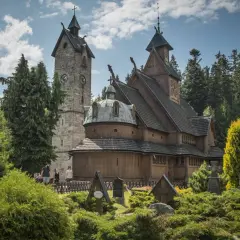 Drewniany kościółek i kamienna wieża z zegarem, otoczone zielenią i nagrobkami. Jedna z głównych atrakcji Karpacz i okolice.